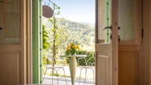 An open door leading to a balcony with a table and chairs, a hanging sign, and a view of a hillside. - Gorgeous home in Castiglion Fiorentino (Castiglion Fiorentino)