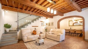 A spacious living area with a staircase, two sofas, a coffee table, and a dining area with a mirror and chandelier. - Gorgeous home in Castiglion Fiorentino (Castiglion Fiorentino)