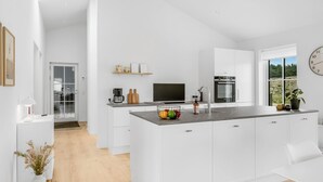 Une cuisine moderne avec des meubles blancs, un îlot central et une grande fenêtre donnant sur l’extérieur.