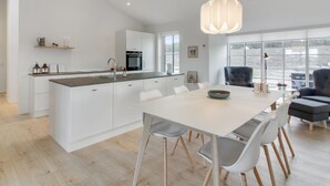 Une cuisine moderne avec des meubles blancs, un îlot central et un coin repas comprenant une table blanche et des chaises grises.