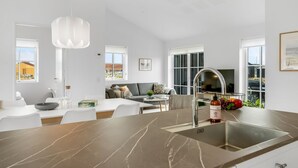 Une cuisine moderne dotée d’un grand îlot central, d’un évier intégré et d’un coin repas avec une table et des chaises blanches.