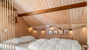 Un dormitorio tipo cabaña de madera con una cama, luces colgantes y cuadros en la pared.