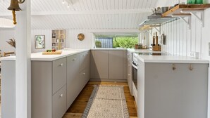 Una cocina moderna con armarios blancos, suelo de madera y vistas a zonas verdes.