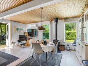 Ein geräumiger Wohnbereich mit Holzbalkendecke, Kamin, Esstisch mit Stühlen, Fernseher und Bücherregal.