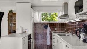 Eine kompakte Küche mit weißen Schränken, einer Mikrowelle, einer Kaffeemaschine und einem Fenster mit Blick auf Grünflächen.