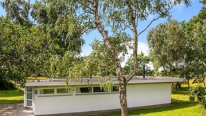 Ein einstöckiges Gebäude mit flachem Dach, einer kleinen Veranda und einem Baum davor.