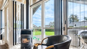 Una sala de estar moderna con una chimenea de leña, ventanas amplias y un sillón cómodo.