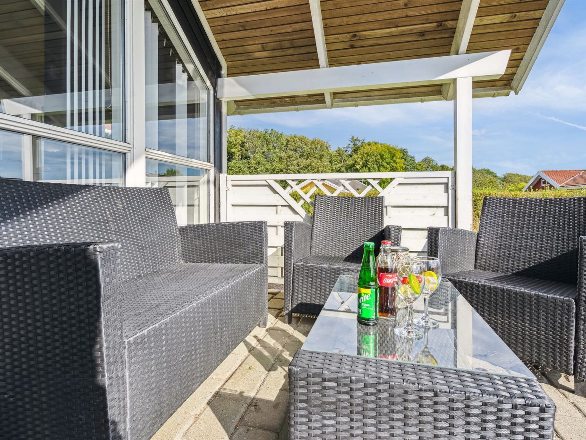 An outdoor patio with wicker furniture, a glass table, and a bottle of Sprite.