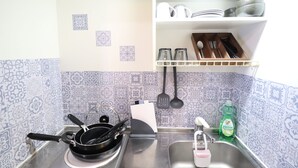 Una cucina con piastrelle decorate, un fornello, un lavello e un portautensili con piatti e bicchieri.