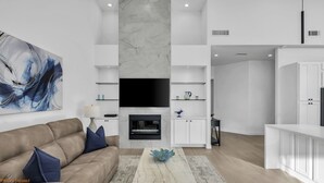 A modern living room with a beige sofa, a flat-screen TV, a fireplace, and a large abstract painting. - Luxury Palm Valley 3BR  3 bath condo (Palm Desert)