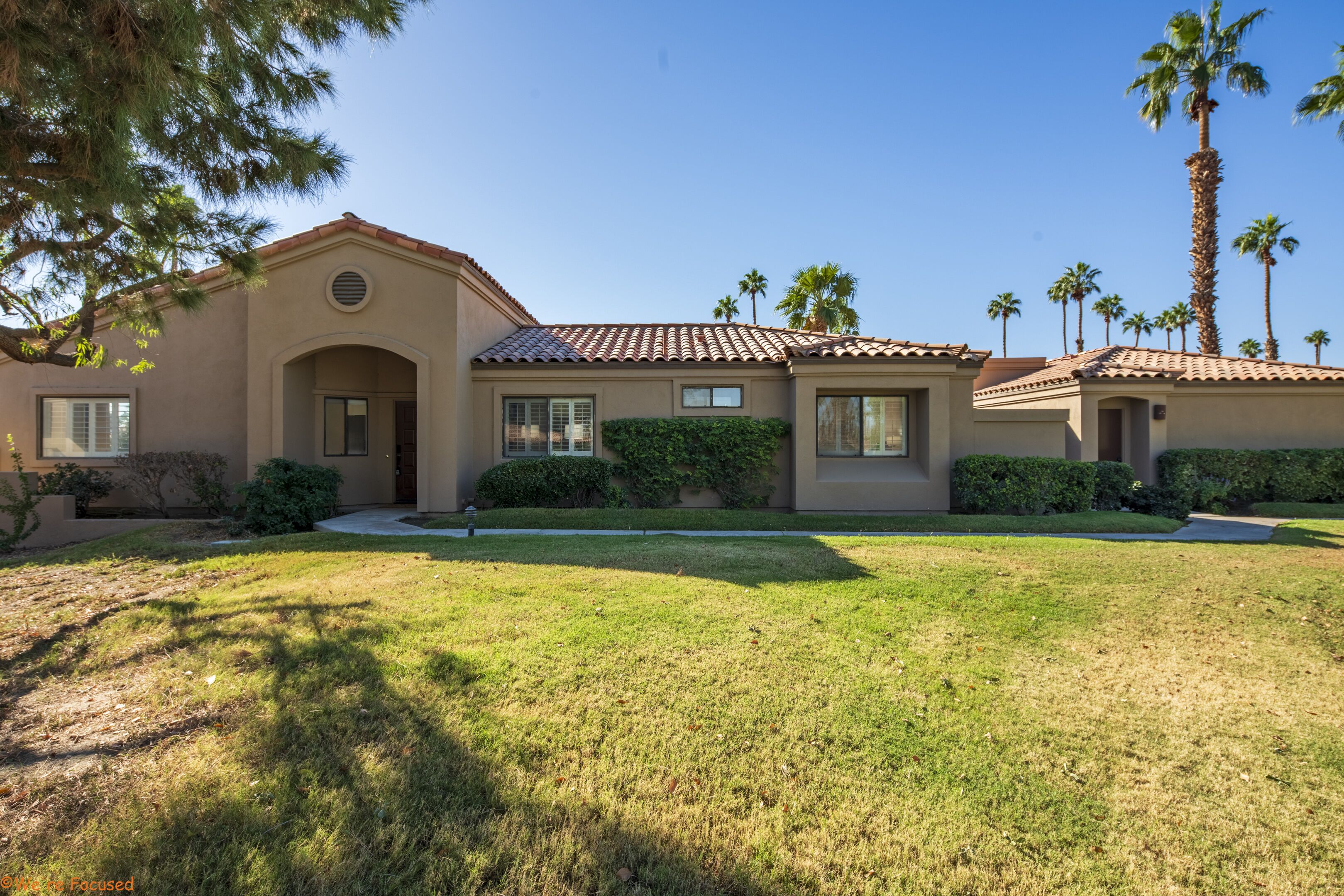 A two-story house with a tiled roof, a front lawn, and palm trees in the background.