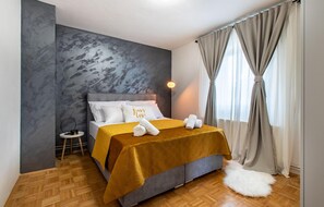 A modern bedroom with a grey textured wall, a bed with white and mustard bedding, a small side table, and a fluffy white rug. - Gorgeous home in Polaca (Polaca)
