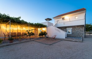 A two-story building with a stone facade and a red-tiled roof. There is a covered outdoor seating area with string lights and chairs. - Gorgeous home in Polaca (Polaca)