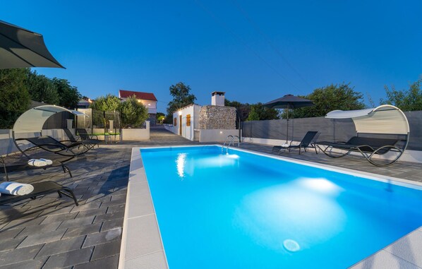 A swimming pool with lounge chairs and umbrellas, surrounded by a stone wall and a house in the background. - Gorgeous home in Polaca (Polaca)