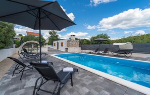 A swimming pool with lounge chairs and umbrellas, surrounded by a stone wall and a covered seating area. - Gorgeous home in Polaca (Polaca)