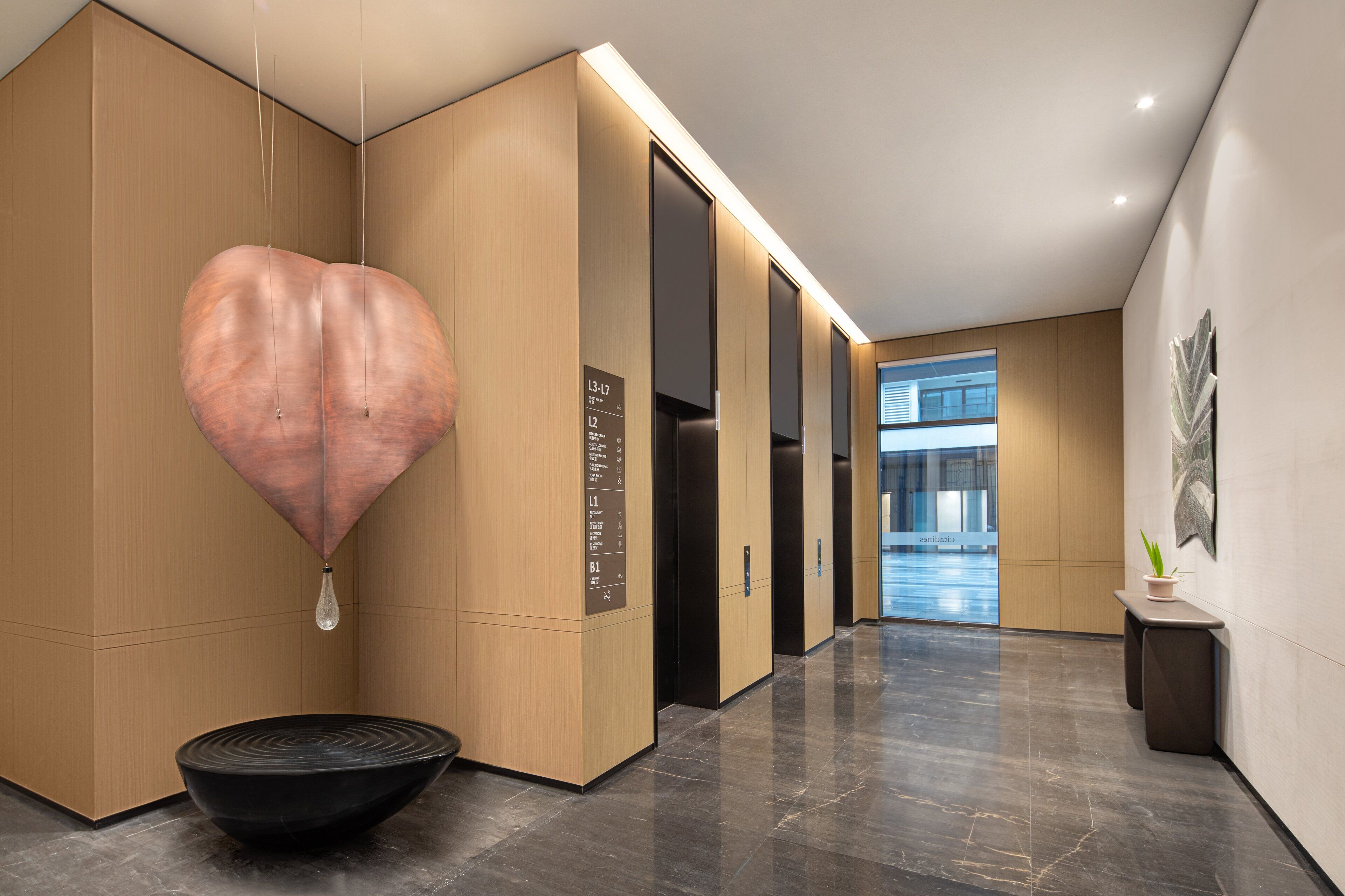 Un vestíbul modern amb una lluminària amb forma de cor, un bol negre i una planta penjant a la paret.