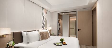 A modern hotel room with a neatly made bed, a bedside table with a lamp, and a door leading to a bathroom.
