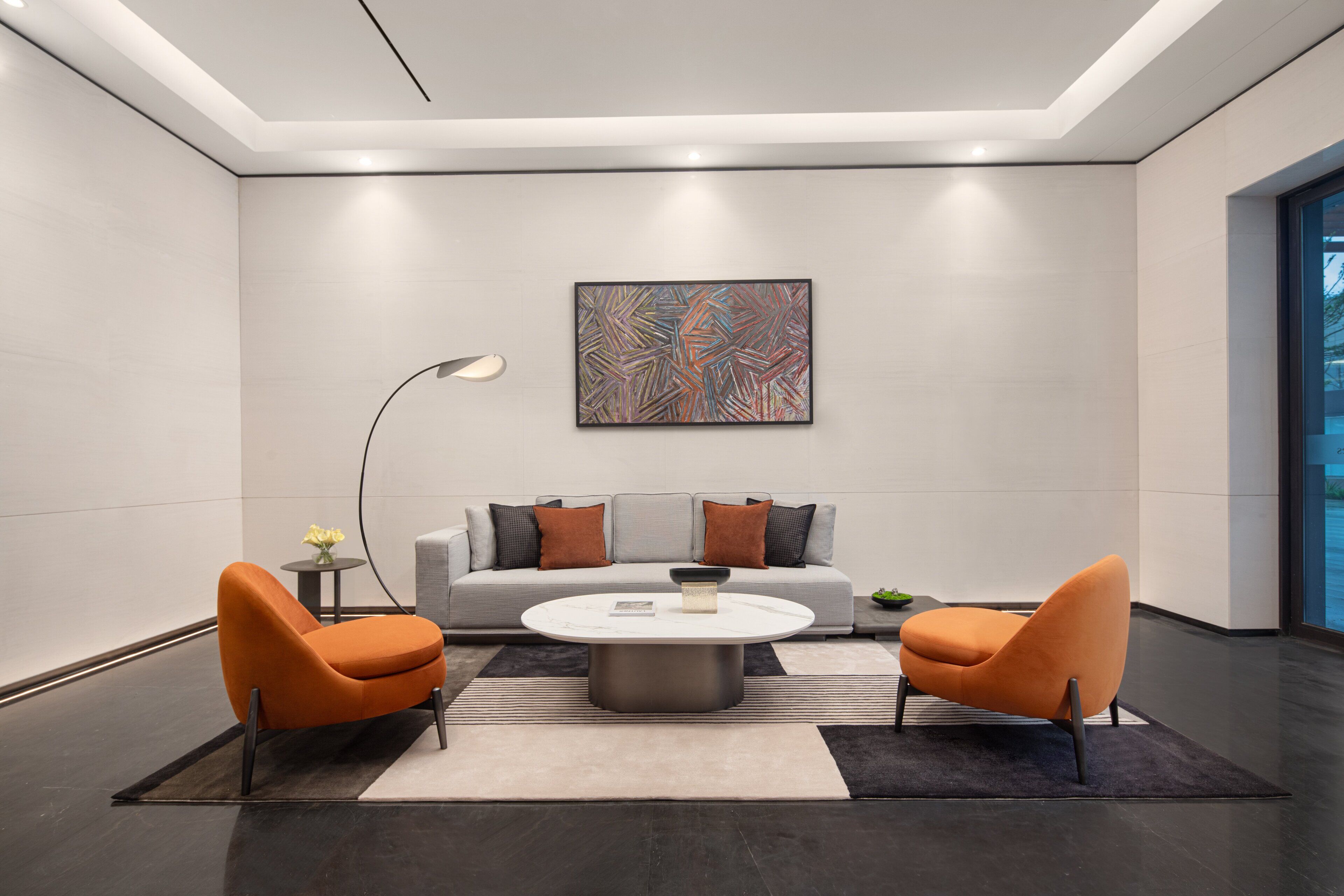 A modern living room with a grey sofa, two orange chairs, a round coffee table, and a floor lamp.