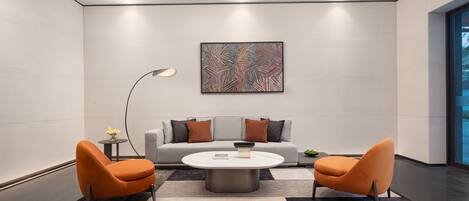A modern living room with a grey sofa, two orange chairs, a round coffee table, and a floor lamp.