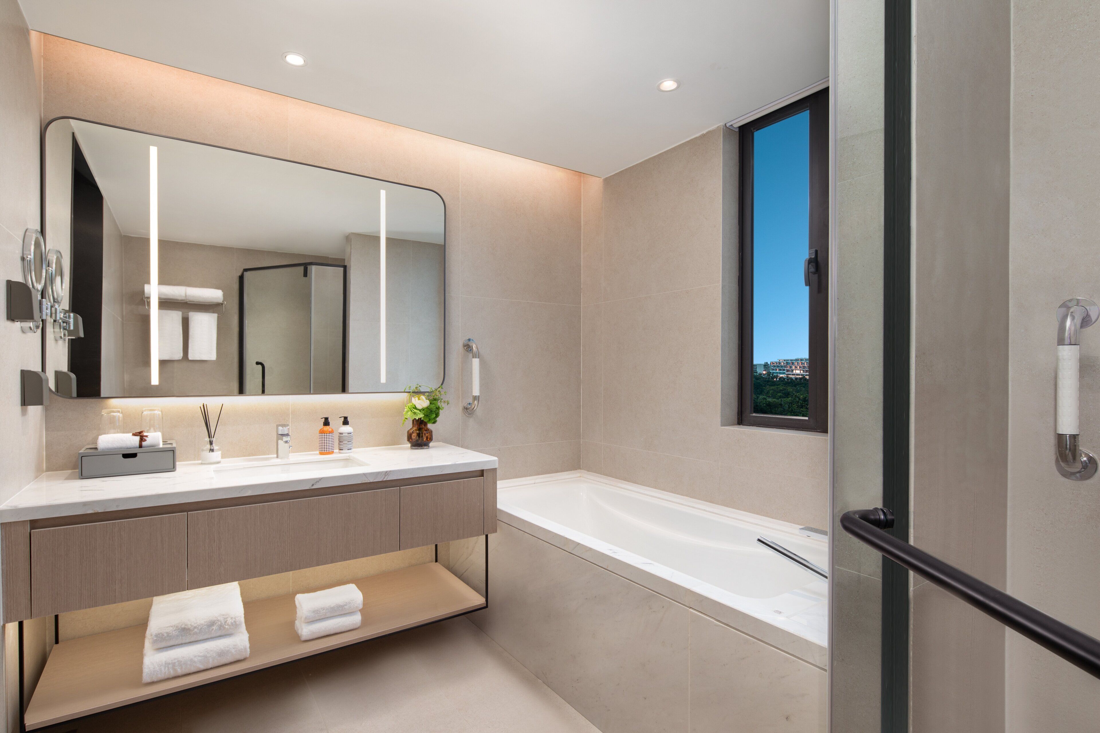 A modern bathroom with a large mirror, a bathtub, and a vanity with a sink and towel rack.