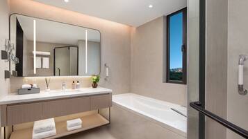 A modern bathroom with a large mirror, a bathtub, and a vanity with a sink and towel rack.
