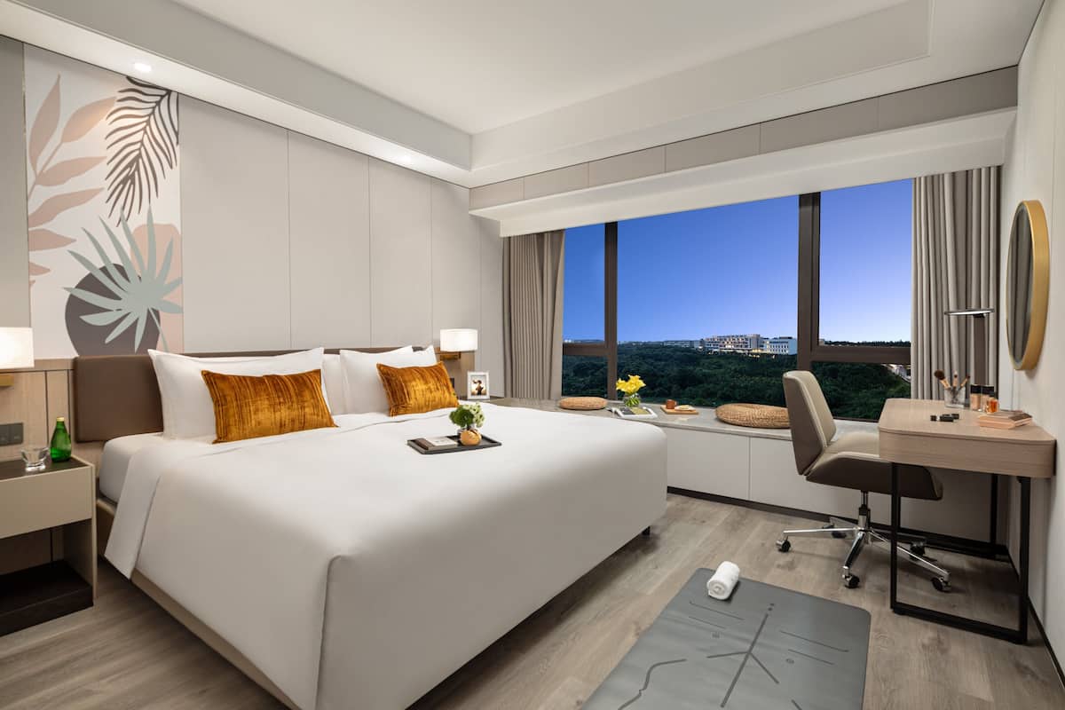 Een moderne hotelkamer met een groot bed, een bureau en uitzicht op de stad.