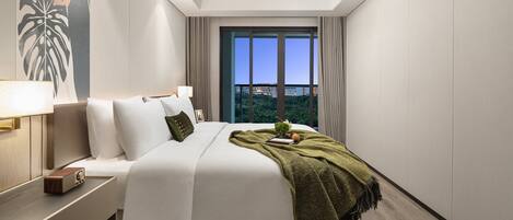 A modern hotel room with a large bed, a nightstand, a lamp, and a view of the city through large windows.