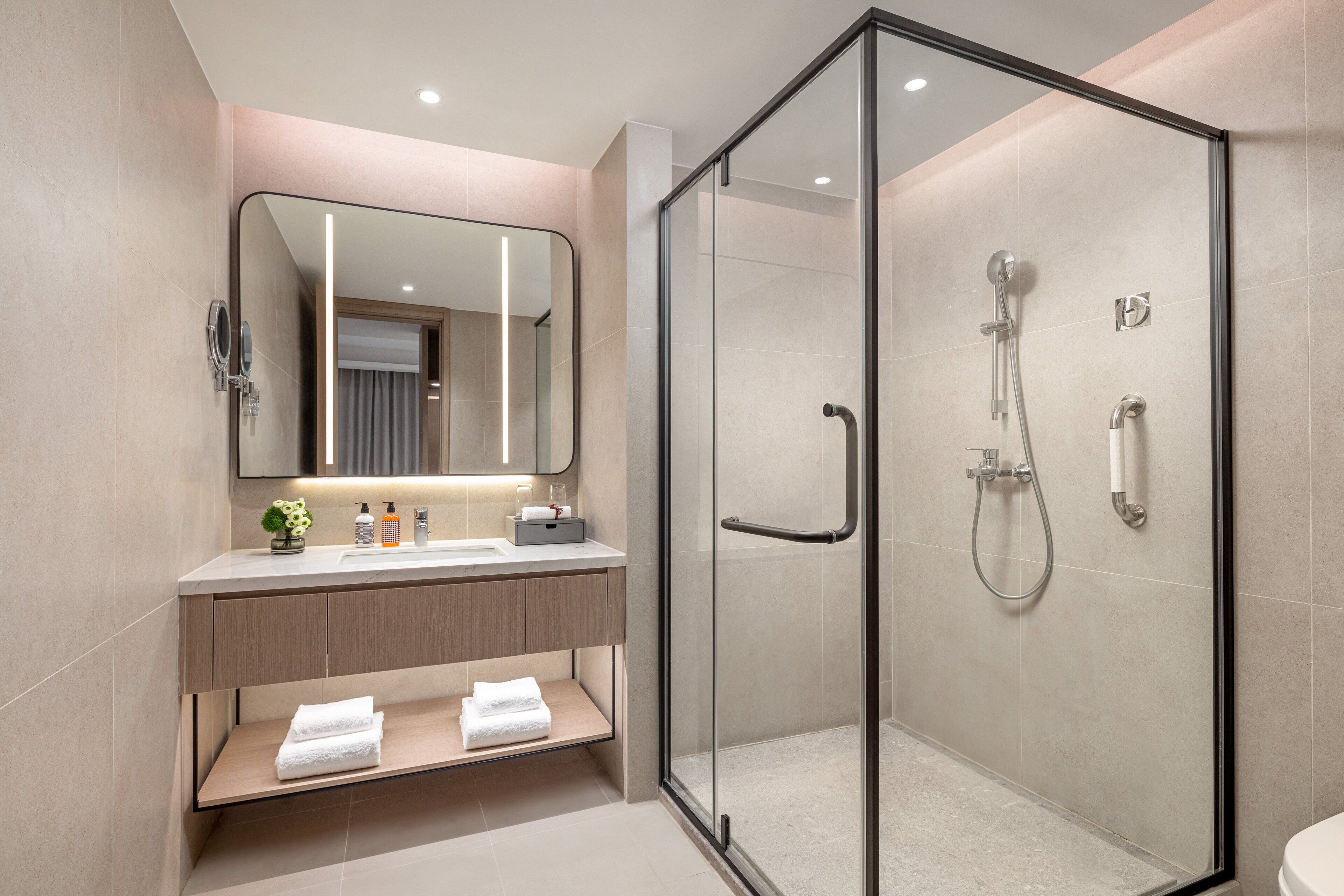 A modern bathroom with a glass-enclosed shower, a vanity with a mirror, and a shelf with towels.