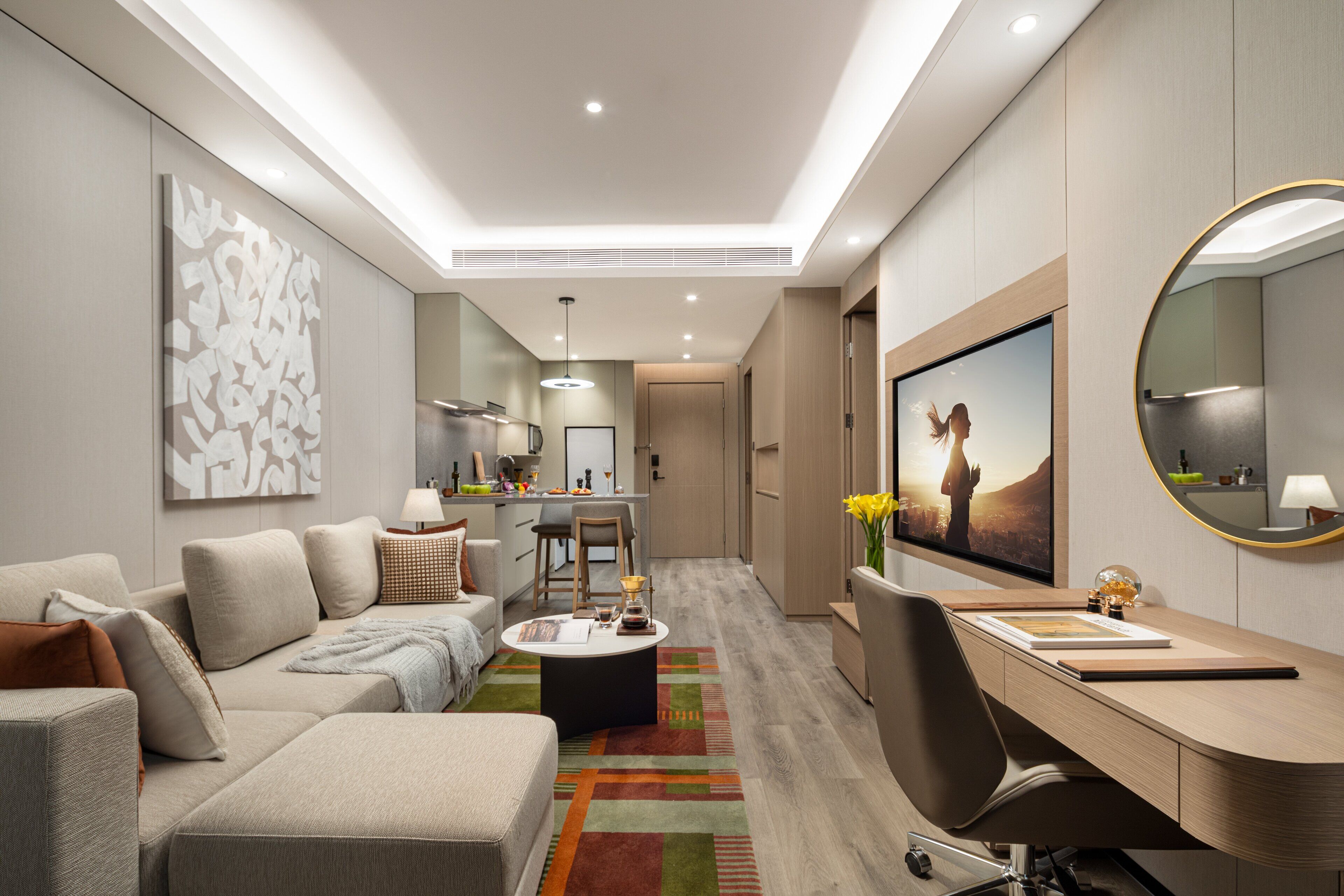 A modern hotel room with a sofa, a desk, a chair, a coffee table, and a large mirror.