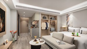A modern hotel room with a sofa, a bedside table, a lamp, a bed, a wardrobe, and a small kitchen area. - Citadines Hope City Boao (Qionghai)