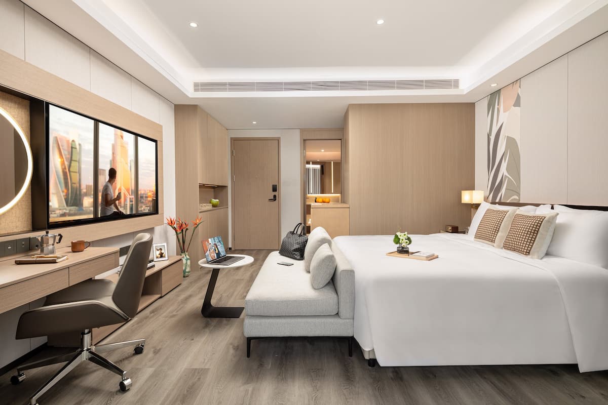 Een moderne hotelkamer met een groot bed, een bureau met stoel, een bank, een klein tafeltje en een spiegel.