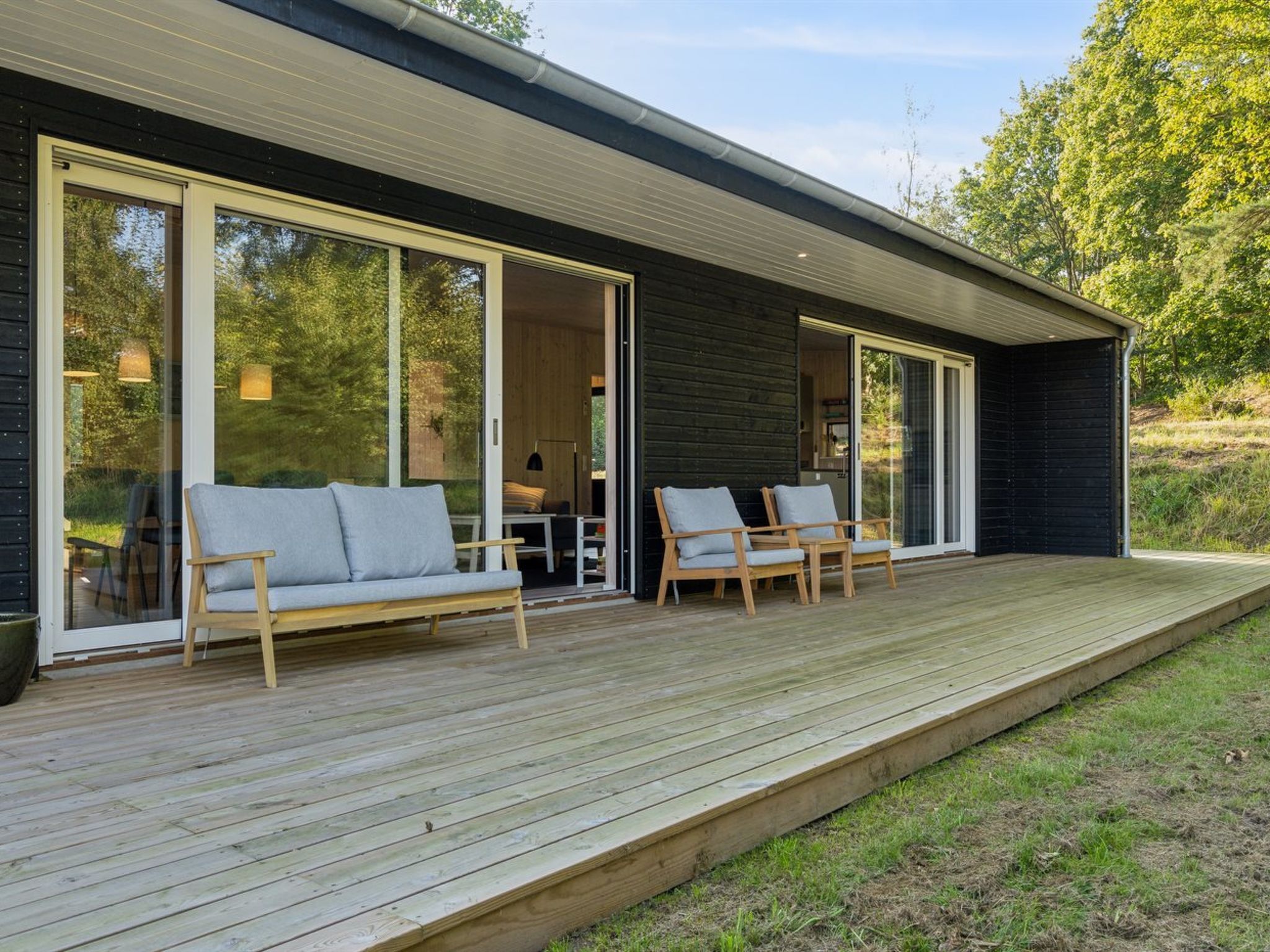 A modern house with a wooden deck, large sliding glass doors, and outdoor seating.