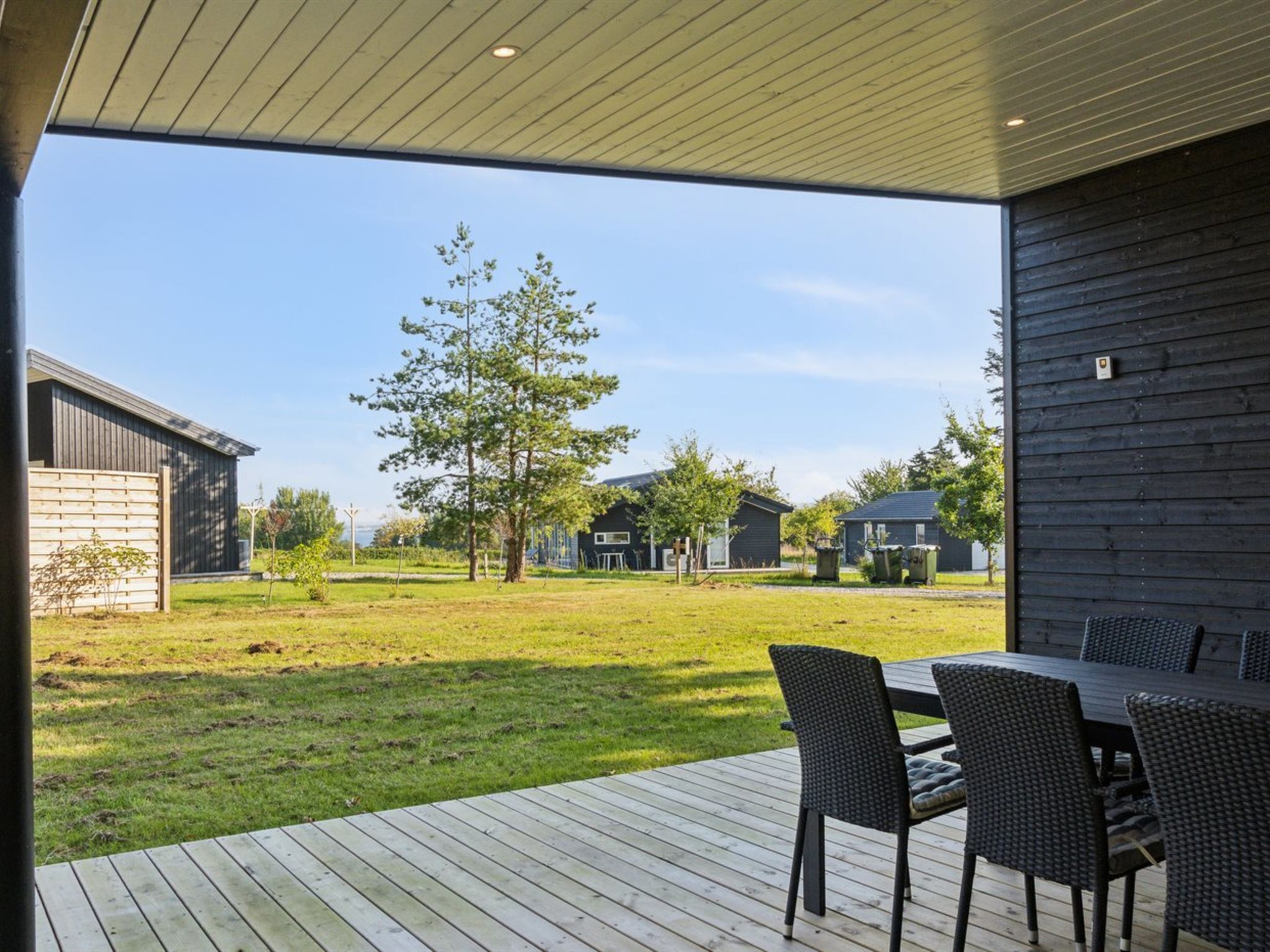 A modern outdoor patio with a wooden deck, a dining table with chairs, and a view of a residential area with houses and trees.