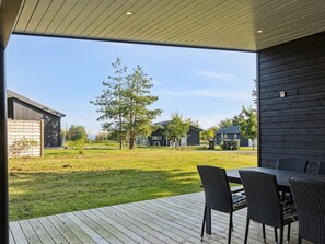 Une terrasse extérieure moderne, dotée d’une plateforme en bois, d’une table à manger avec des chaises et offrant une vue sur un quartier résidentiel avec des maisons et des arbres.