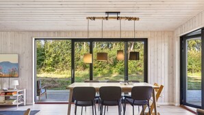 A modern dining area with a wooden table and chairs, large windows, and a view of greenery outside. - "Uma" - 1.5km from the sea by Interhome (Knebel)