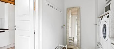 A laundry room with a washing machine, a drying rack, and a mirror on the wall.