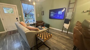 A living room with a sofa, a coffee table, a TV, and a chessboard. - Charming 1920’s shotgun in southern Indiana, minutes from downtown Louisville  (New Albany)