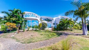 A modern, white, multi-level building with unique circular windows and balconies, surrounded by lush greenery and palm trees. - Lion Fish Retreat (Placencia)