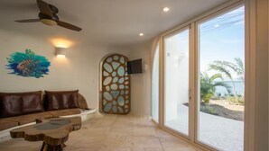 A spacious living area with a large window, a ceiling fan, a wooden coffee table, and a decorative wall piece. - Lion Fish Retreat (Placencia)