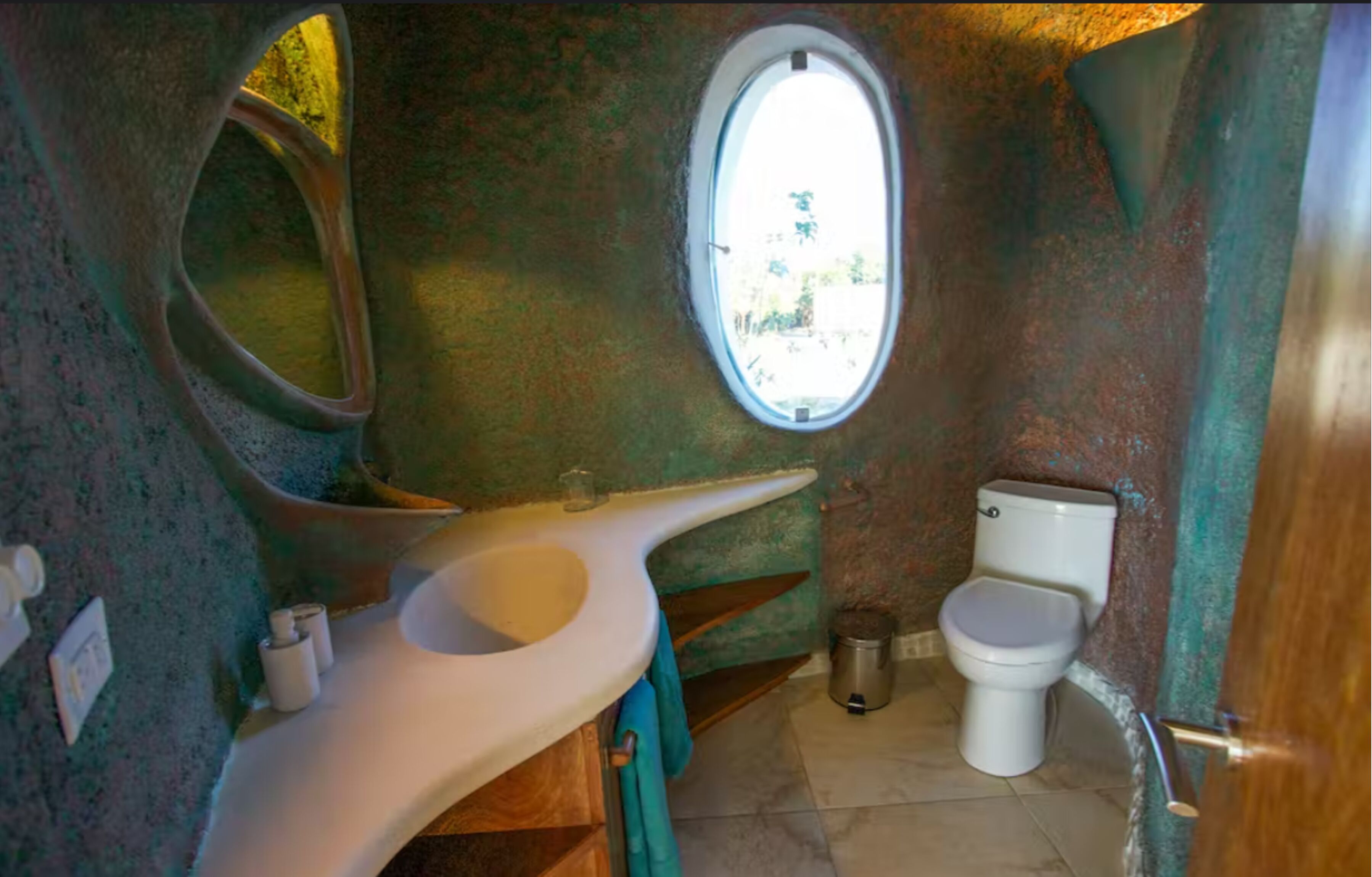 A bathroom with a unique architectural design, featuring a curved sink, a small window, and a toilet.