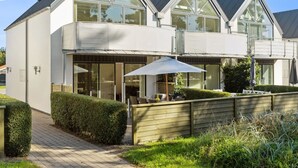 Una casa moderna de dos pisos con amplios ventanales, un patio cubierto y un jardín bien cuidado.