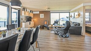 Un salon moderne avec une cheminée, un coin repas avec une table et des chaises, et un espace détente avec des canapés et un téléviseur.