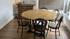 Un comedor con una mesa redonda de madera rodeada de sillas, una pequeña mesa auxiliar de madera con una lámpara y un equipo de aire acondicionado fijado a la pared.