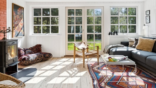 A cozy living room with a fireplace, large windows, a sofa, and a patterned rug.