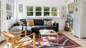 A cozy living room with a dark grey sofa, a wooden chair, a coffee table with a tray of fruit, and a colorful rug.