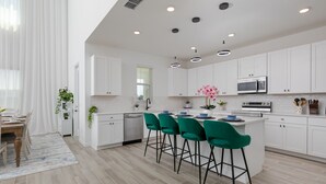 A modern kitchen with white cabinets, a central island with green bar stools, a microwave, and a dishwasher.