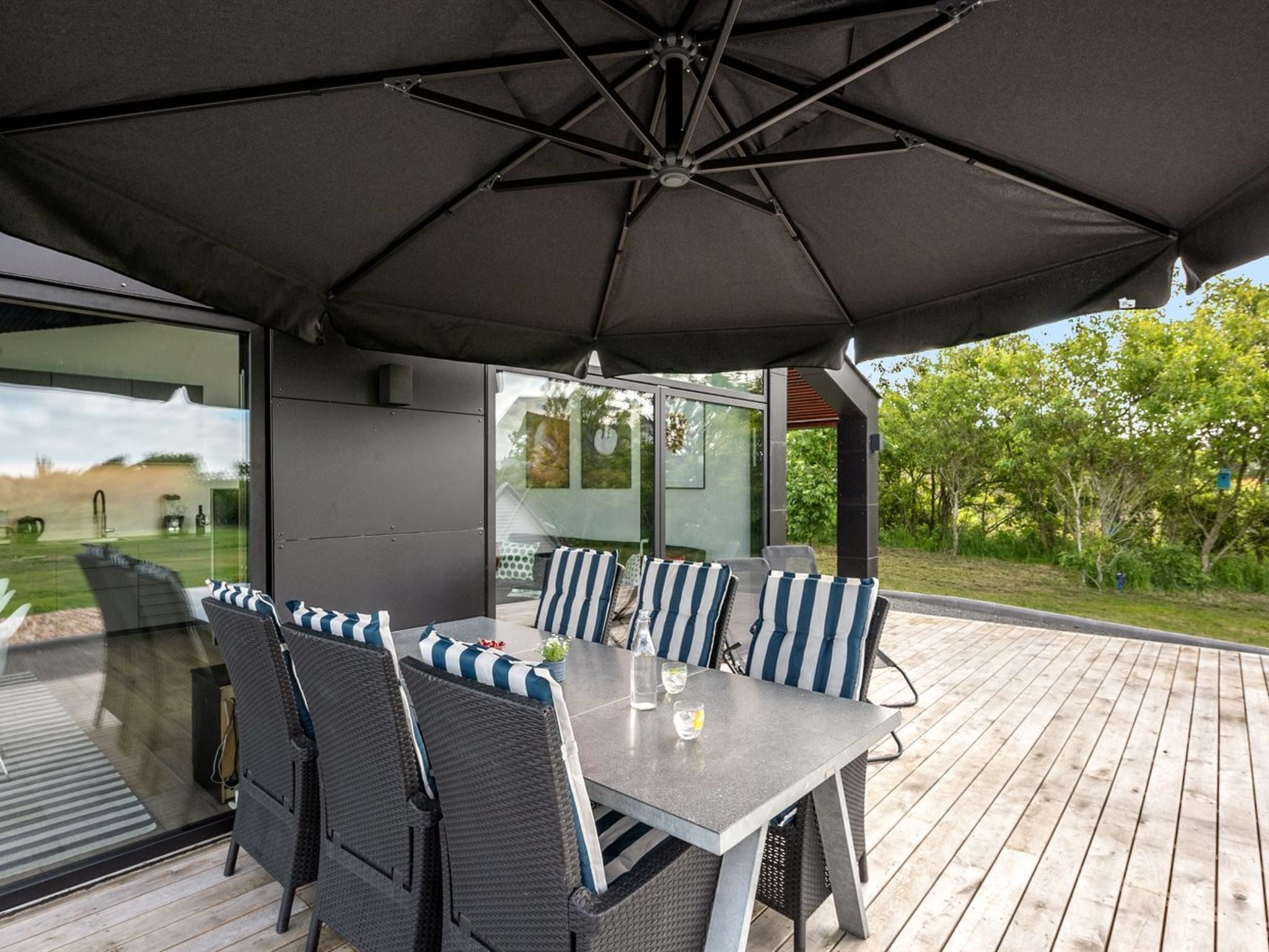 An outdoor patio with a table and chairs, a large umbrella, and a glass wall overlooking a garden.