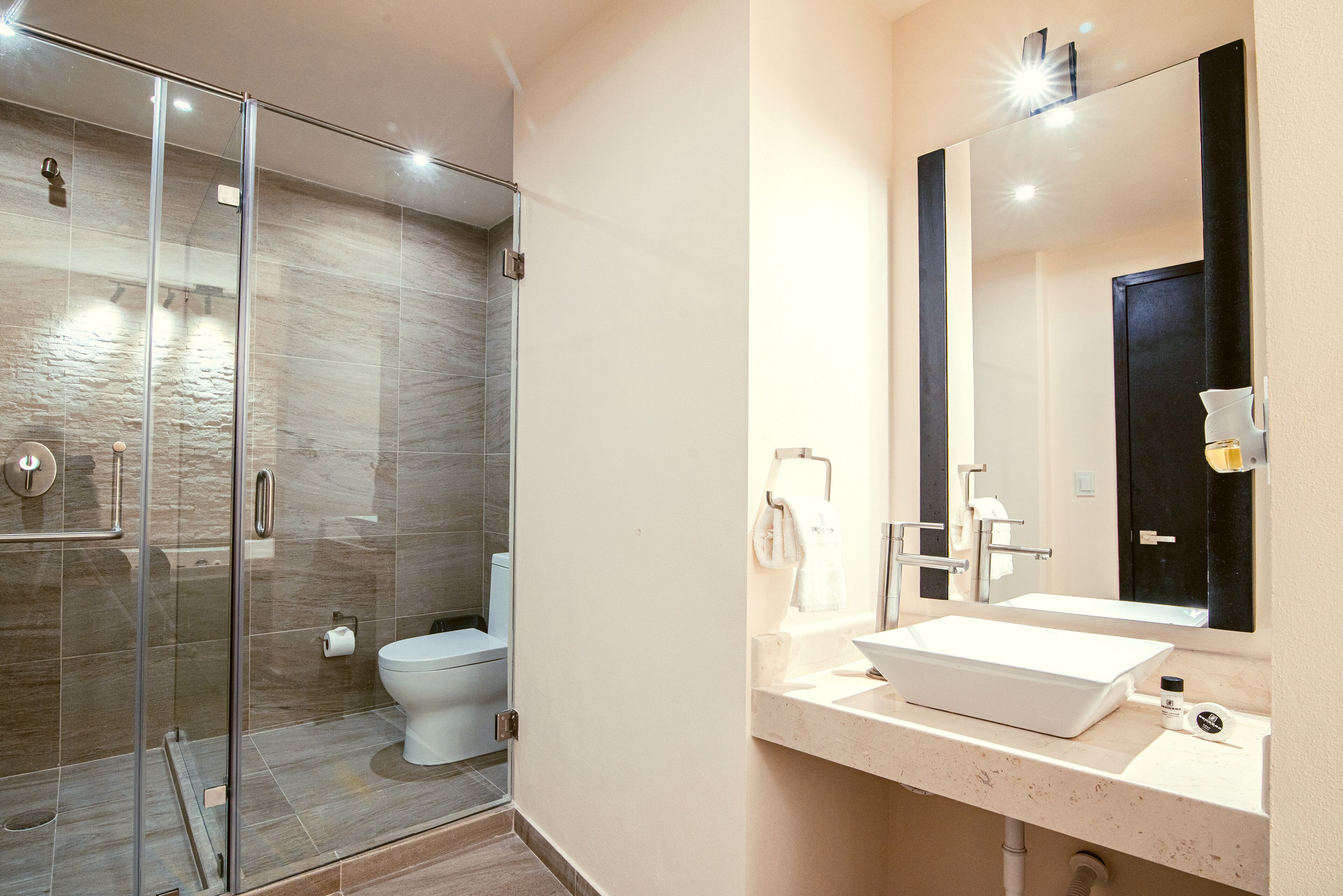 Un baño moderno con ducha de vidrio, lavamanos blanco y un espejo grande.