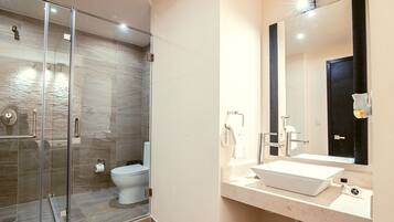 Un baño moderno con ducha de vidrio, lavamanos blanco y un espejo grande.