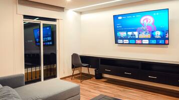 Una sala de estar moderna con un televisor de pantalla plana montado en la pared, un sofá gris, una mesa de centro de madera y un cubo de basura negro.